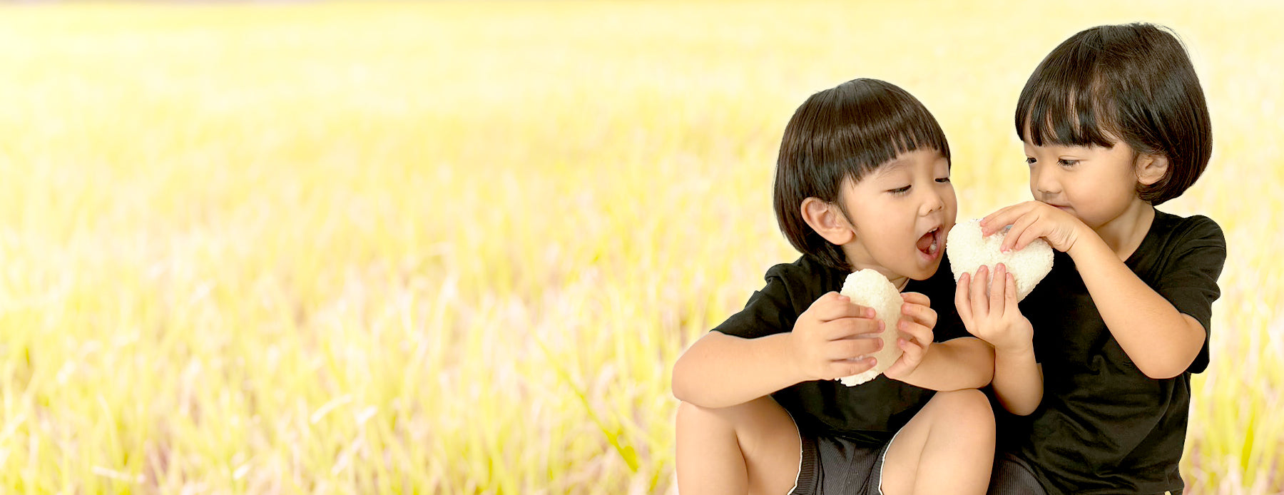 田んぼでおにぎりを食べる子ども